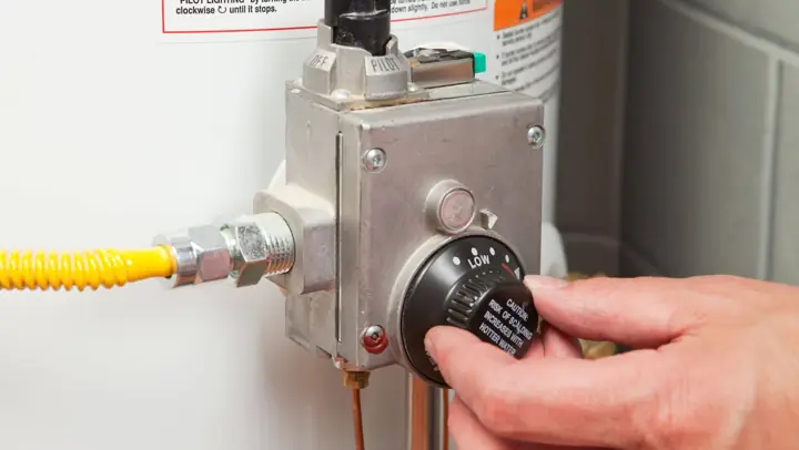 Plumber adjusting the thermostat dial on a gas water heater